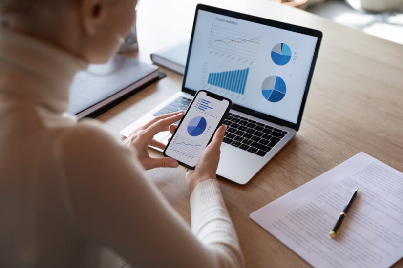 Woman Looking At Charts On Her Phone And Laptop