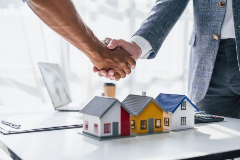 Two Men Shaking Hands And Some House Models On The Table